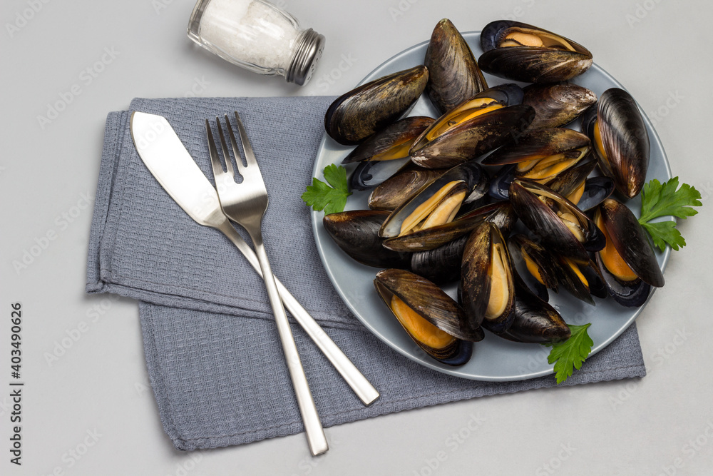 Mussels in gray plate. Fork with knife on gray napkin Mussels in gray plate. Fork with knife on gray napkin