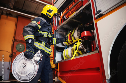 Konstfotografi Firefighter in protective uniform with helmet on head checking on hoses before intervention while standing in fire station