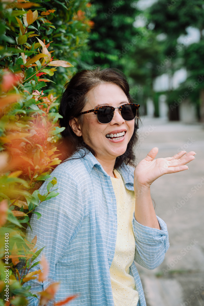 Portrait of senior woman wearing sunglasses standing by plant wall. Portrait of senior woman wearing sunglasses standing by plant wall.