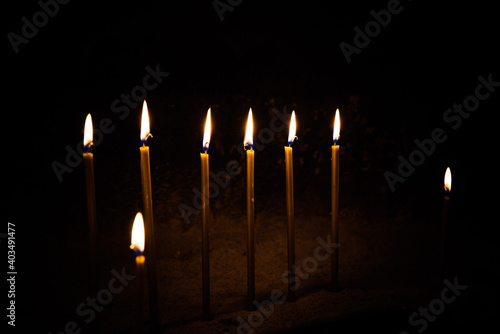 yellow wax candles burn in church on black background