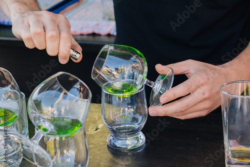 The bartender pours green absinthe into beautiful wine glasses and sets them on fire at a street party.