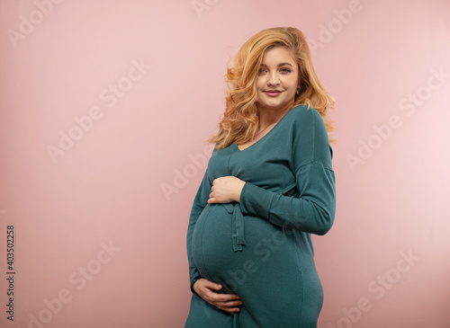 Portrait of a beautiful pregnant woman in a green dress on a pink background