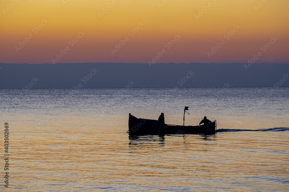 Silhouette of two fishers on a boat fishing at sunset
