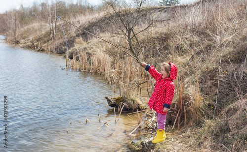 A little girl catches a fish. A lonely happy little child is fishing from the beach of a lake or pond.Photo of children pulling a fishing rod during a weekend fishing trip.