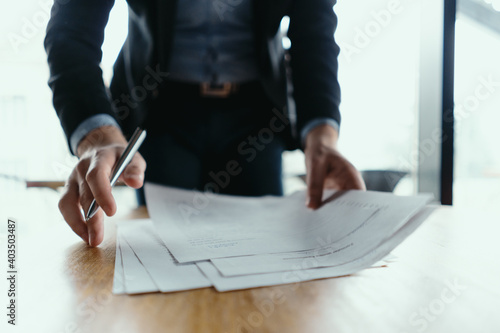 Close up hands signing documents in a modern office with window in background. Pen in hand, papers on the wooden desk, futuristic background. photo