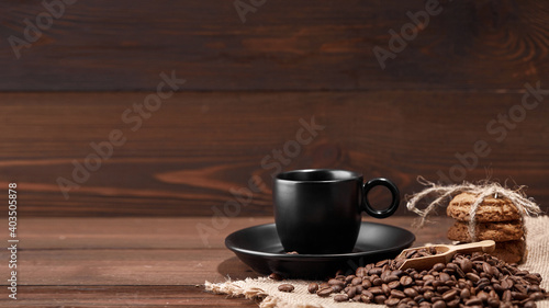 A cup of hot drink on roasted coffee beans and oatmeal cookies on a wooden kitchen table on woven burlap with copy space to decorate the text