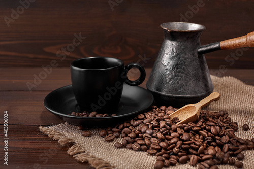 Close up of a cup of hot drink a wooden ladle with roasted coffee beans on a wooden kitchen table on a woven burlap with copy space to decorate the text