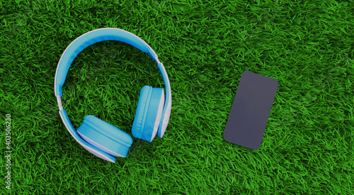 Close up blue wireless headphones and phone on a green background, top view