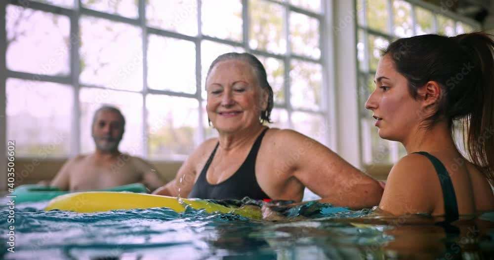 Instructor helping senior woman aerobics class with pool noodle