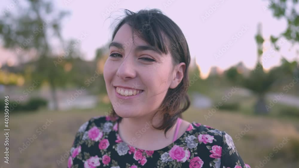 A beautiful white woman Latina in a dress with roses looks towards the camera and smiles in the foreground and surrounded by a beautiful place with green areas A beautiful white woman Latina in a dress with roses looks towards the camera and smiles in the foreground and surrounded by a beautiful place with green areas