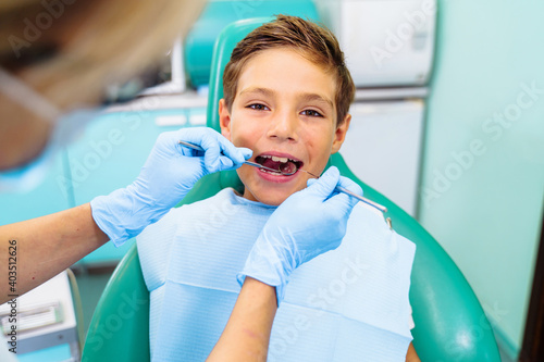 A small patient with an open mouth at a dentist appointment in a modern clinic. Hands of unrecognizable pediatric dentist doing examination procedure for smiling cute boy in hospital