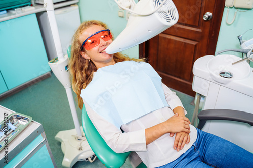 Teeth whitening. A patient in protective glasses from the rays in the chair at the dentist. Preventive examination of the oral cavity. Installing the mouth spacer. At the dentist appointment