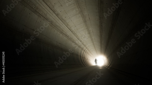 Concept or conceptual dark tunnel with a bright light at the end or exit as metaphor to success, faith, future or hope, a black silhouette of walking man to new opportunity or freedom 3d illustration