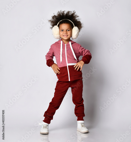 Happy smiling Afrio girl posing in warm headphones and sportswear. The child is posing near the place for the text. The concept of children clothing for sports, training and walking outdoors.