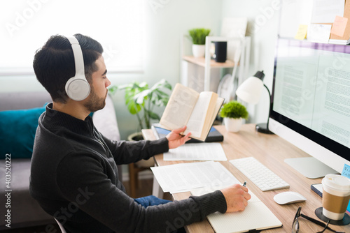 Quadro su tela Young man translating a book at his home office desk
