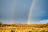 Rainbow over country side and small asphalt road, West of Ireland. Fall and winter season. Blue cloudy sky