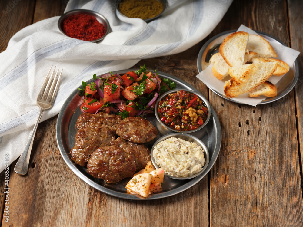 meatballs with mezes and toasted bread and a fork on a metal plate on wooden background
