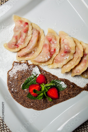Konstfotografi Vareniki with strawberries, mint on a large white plate, on food mat - bamboo mat background Next to the knife and fork - cutlery