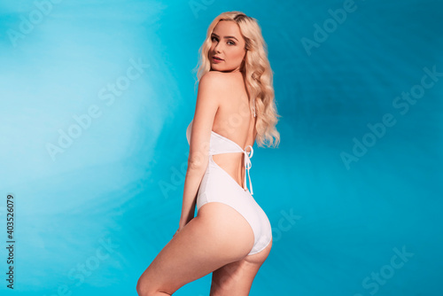 Beautiful fashionable young blonde woman in a studio. Wearing white swimsuit  big straw summer hat. Spring  summer beach fashion photo  portrait.