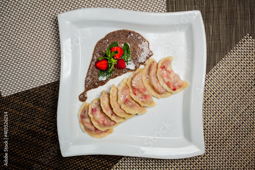 Canvastavla Vareniki with strawberries, mint on a large white plate, on food mat - bamboo mat background Next to the knife and fork - cutlery