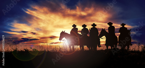 Foto Group of cowboys on horseback at sunset