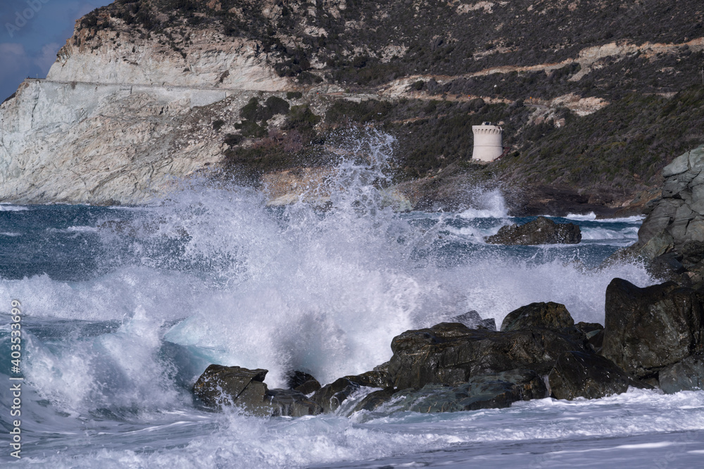 Big wave breaking on some rocks and the Tour d'Albo, on the Corsican coastline 