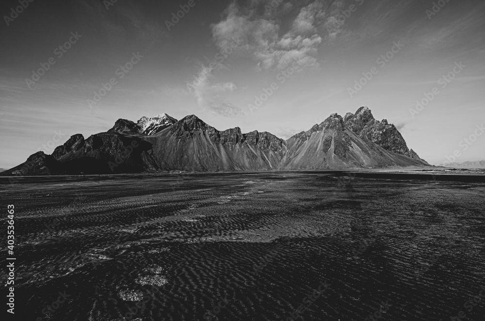 Black and white view of Vestrahorn  in Iceland, part of the sandy beach is frozen over. 