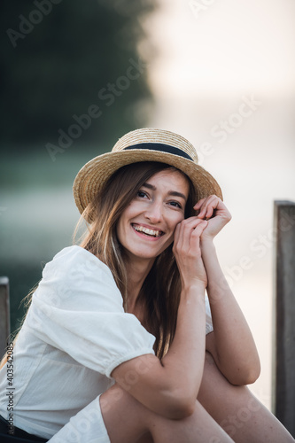 Portrait of a happy caucasian woman in a white dress and hat outdoors sitting and smiling.