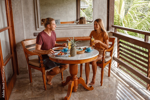 Couple On Summer Terrace Having Breakfast in tropical conutry, palm trees behind the balcony