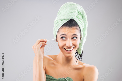 Beautiful young girl posing with towels after having a bath, holding cotton ear stick. Funny smiling face expression