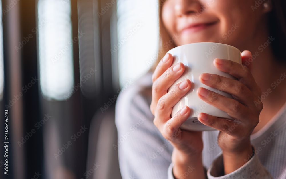 Closeup image of a beautiful young asian woman holding and drinking hot coffee in cafe - obrazy, fototapety, plakaty 
