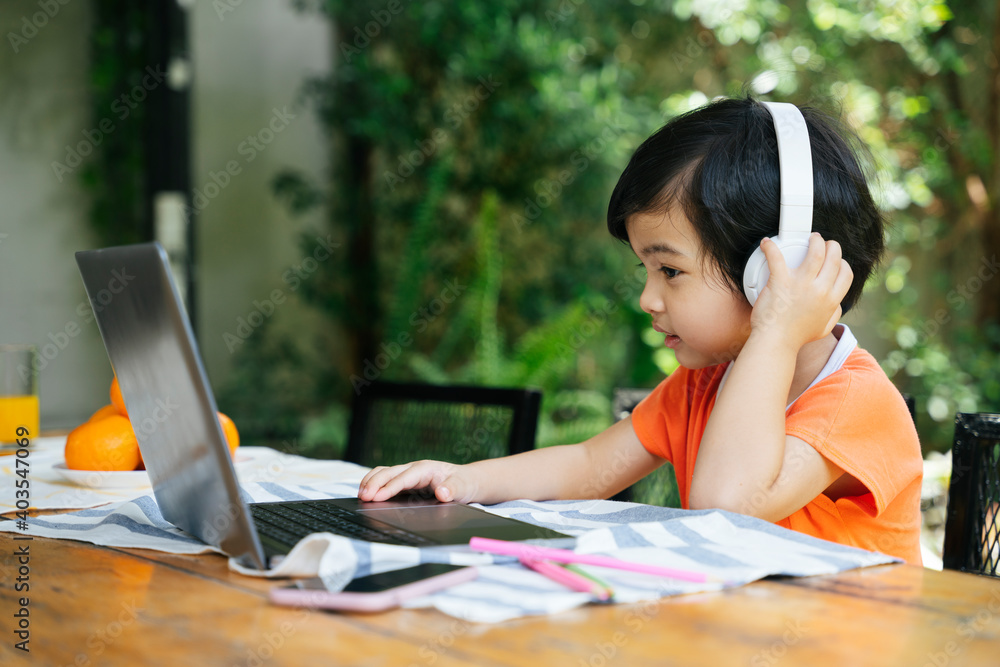 Asian kid wear headphone using laptop outdoors at yard. Asian kid wear headphone using laptop outdoors at yard.