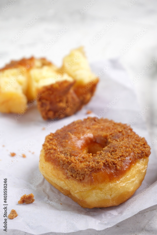 Donat or Donut or Doughnut as circle with hole sweet bread topped with caramel and biscuit crumbs. Selective focus, white shiny background