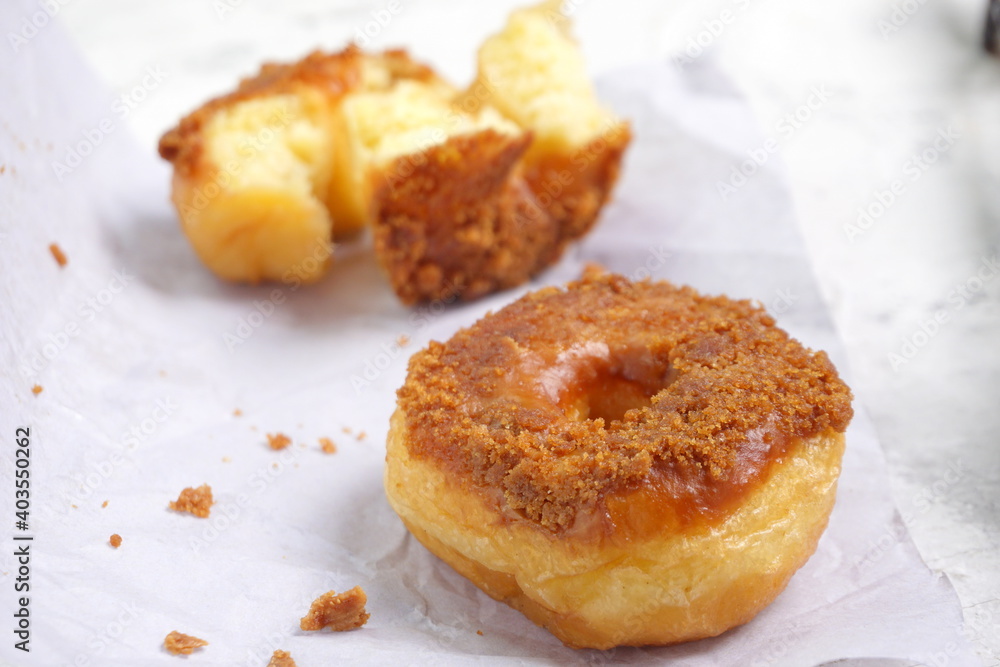 Donat or Donut or Doughnut as circle with hole sweet bread topped with caramel and biscuit crumbs. Selective focus, white shiny background