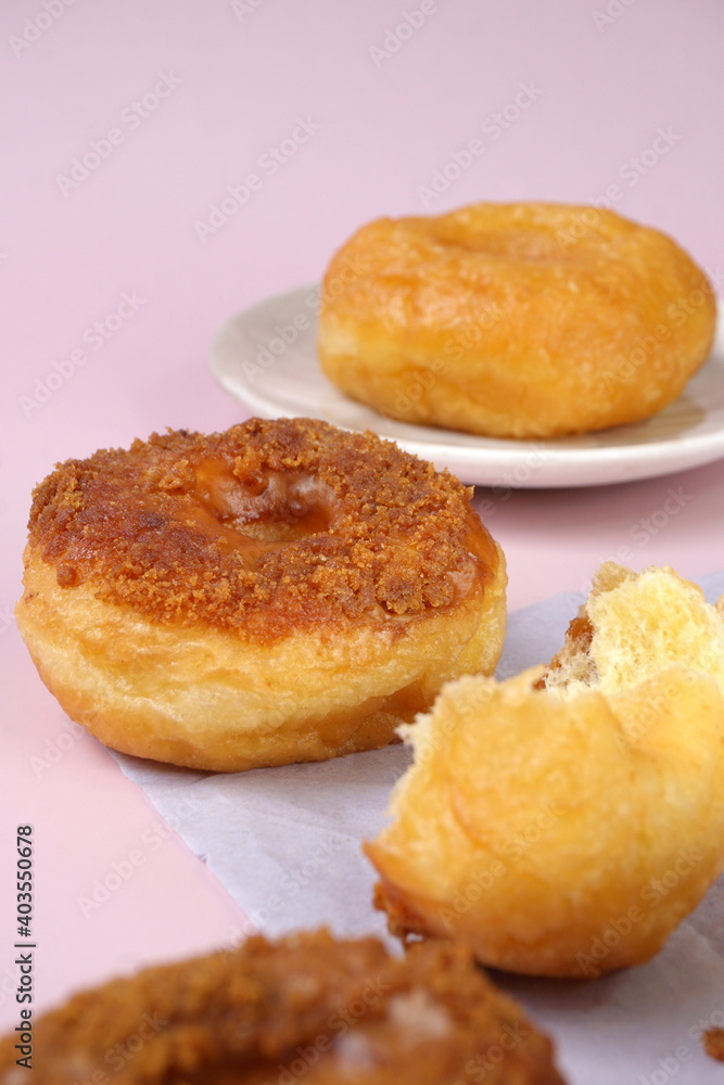 Grainy Donat or Donut or Doughnut with caramel and Lotus biscuit crumbs. Selective focus, pink pastel background