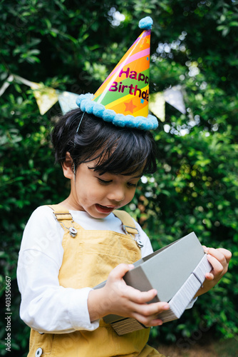 Asian black hair kid wear party hat holding present gift box at yard.