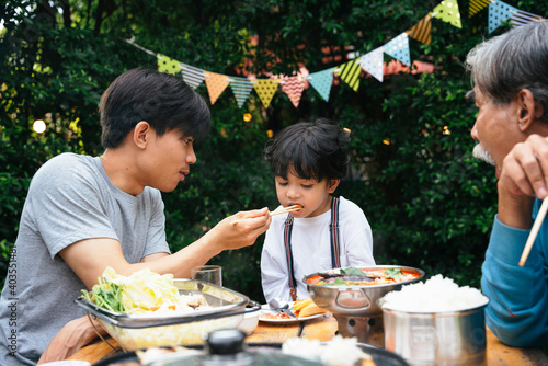 Fotografie, Tablou Asian daddy feeding food to son in dinning party outdoor.