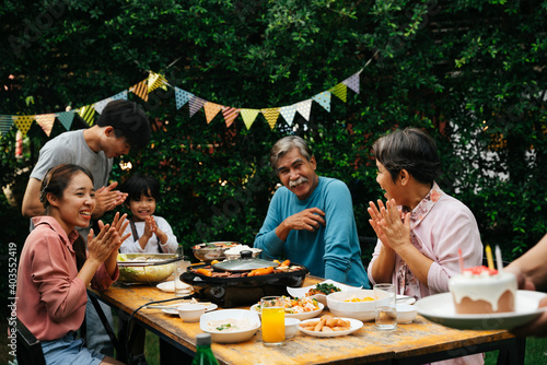 Asian family celebrate birthday party for a kid with cake at yard.