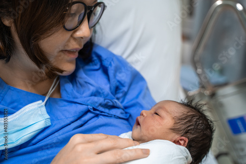 asian female parent holding newborn baby with care on bed at hospital.