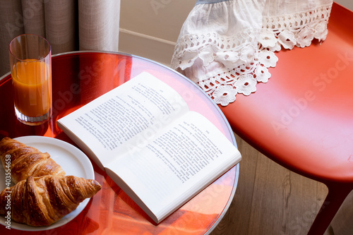 Red table and chair with little dress and breakfast, open book croissants and orange juice