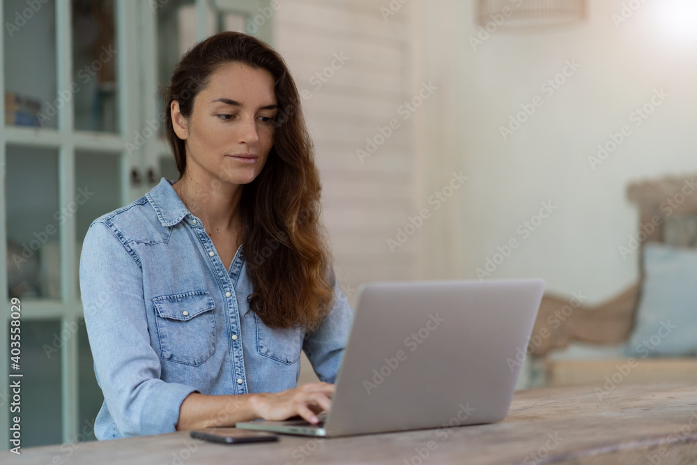 Thinking woman with phone and computer sitting on the table. Working at home. Home blurred background.