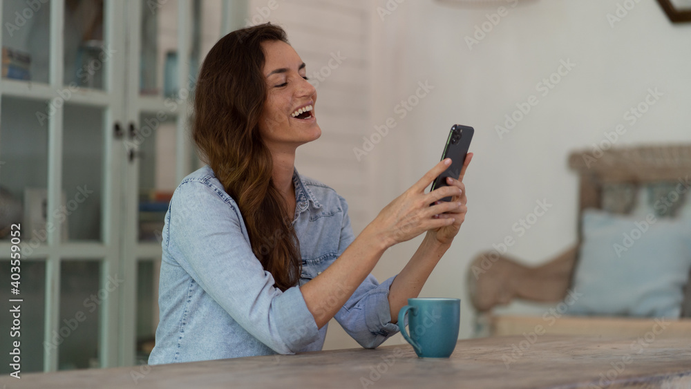 Smile woman typing messages by phone on the table with cup of coffee at home Smile woman typing messages by phone on the table with cup of coffee at home