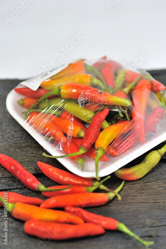 Some red chilies on a black wooden base and a bunch of red chilies in a plastic box on a white background