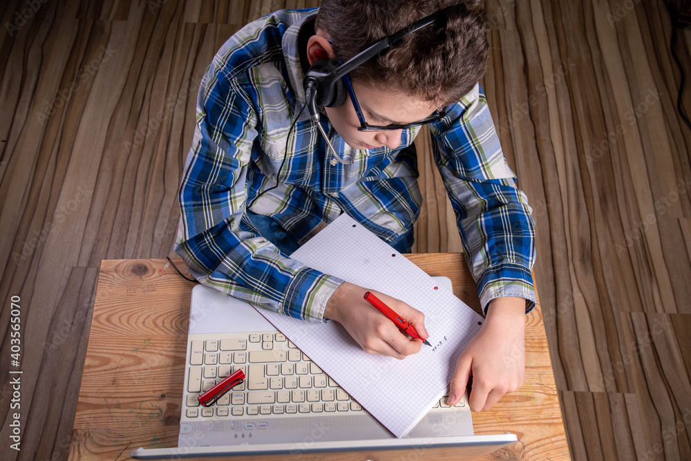 Boy with shirt and glasses makes notes on laptop with fountain pen Boy with shirt and glasses makes notes on laptop with fountain pen