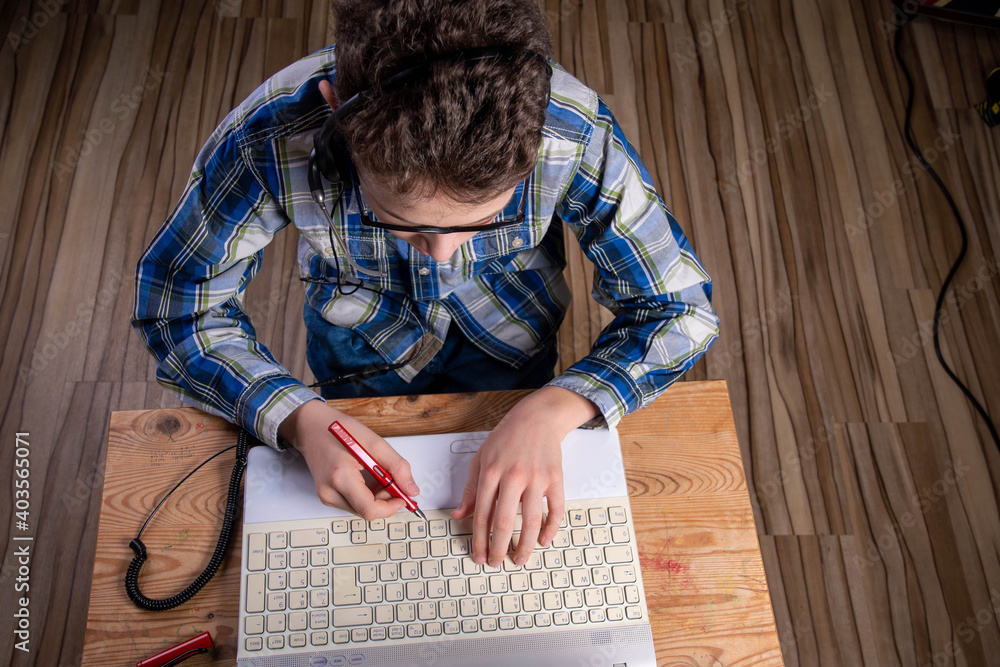 Boy with shirt and glasses makes notes on laptop with fountain pen Boy with shirt and glasses makes notes on laptop with fountain pen