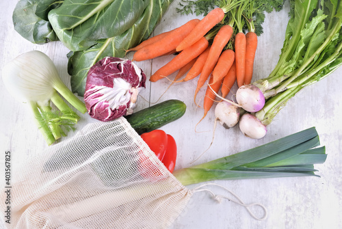 vegetables in a reusable  bag  among other  fresh vegetables  on a white table