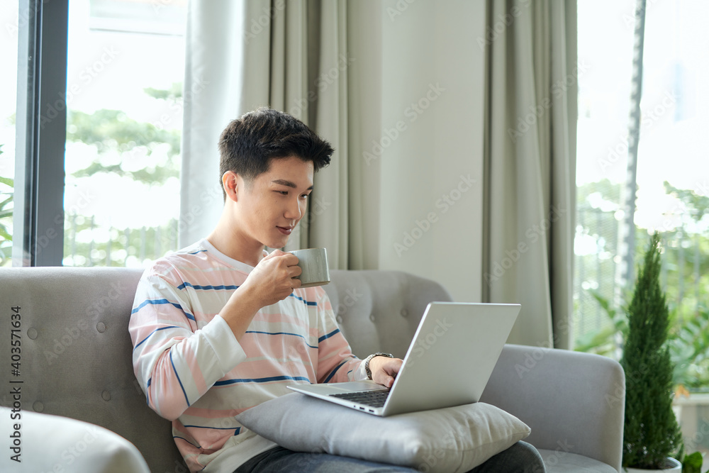 Man works for laptop. He rejoices in the search result, holding a cup of coffee Man works for laptop. He rejoices in the search result, holding a cup of coffee