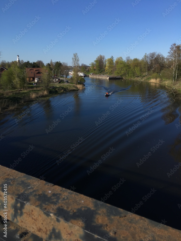 The boat floats on the river. Boat with a motor on the blue surface of the water. Sunny weather and calm river. Village houses stand on the river bank