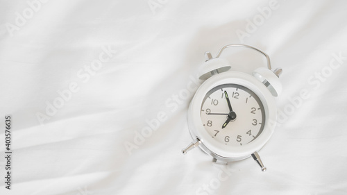 white alarm clock on messy white bed sheet , early wake up , awaken or reminder concept with copy space