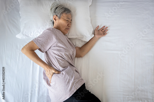 Foto Sad asian senior woman touching hip on her bed,problem of pain while sleep feel